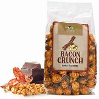 A clear plastic bag labeled "Bacon Crunch" is filled with caramel popcorn. Slices of bacon and pieces of chocolate are placed beside the bag.