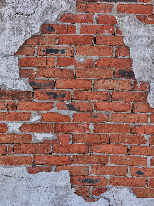Red brick wall with patches of gray plaster partially covering the surface, revealing exposed bricks in irregular shapes.