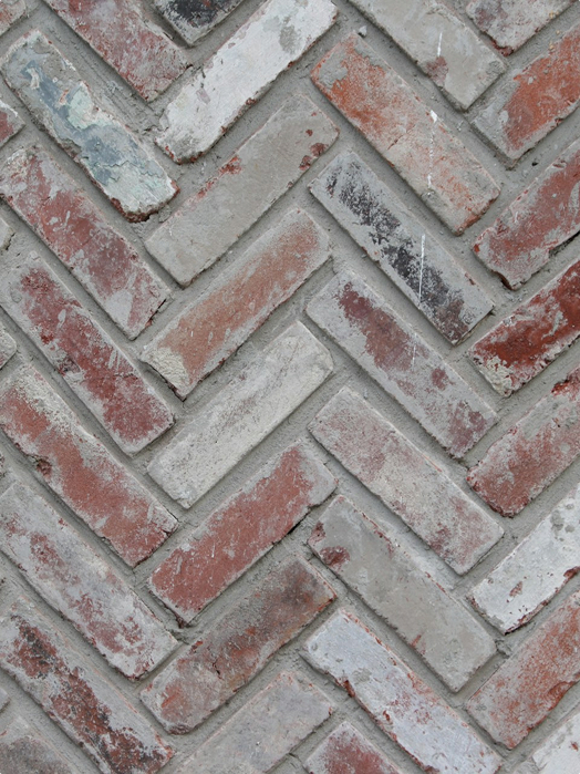 Close-up of a herringbone pattern made with weathered red and gray bricks, with mortar visible between the bricks.