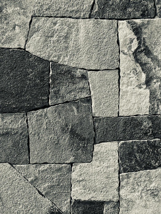 Close-up of an unevenly arranged stone wall made of rectangular and irregular light and dark gray stones.